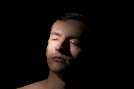 Portrait of a young man with closed eyes on a black backgroundの写真素材