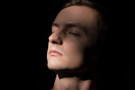 Portrait of a young man with closed eyes on a black backgroundの写真素材