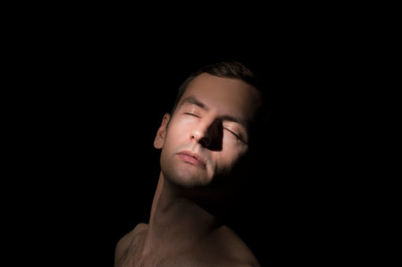 Portrait of a young man with closed eyes on a black backgroundの写真素材