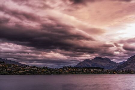 storm clouds over lake wakatipu with kelvin heights in the distance. Sunlight covered in stormy...