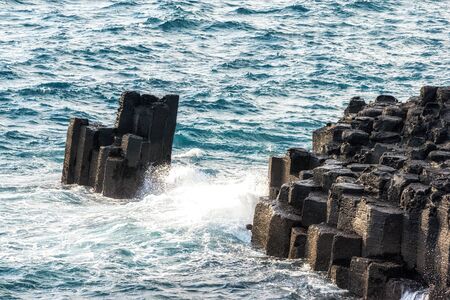 waves hitting the side of daepo jusangjeolli cliff stone pillars in jejudo, south koreaの写真素材