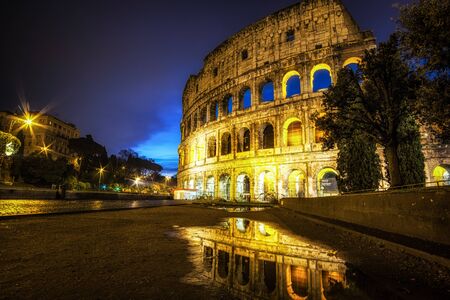 Famous Colosseum reflecting off the small rain puddle on mud. Taken at duskの写真素材