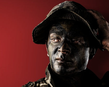 young soldier face with jungle camouflage on red backgroundの写真素材