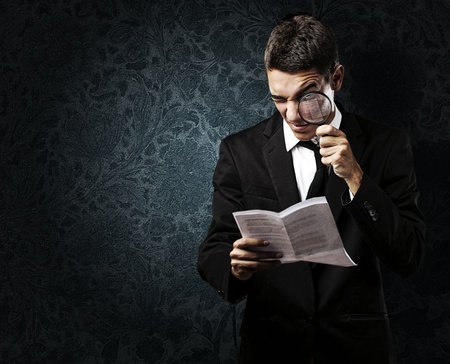 portrait of handsome young man reading a contract through a magnifying glass against a grunge backgroundの写真素材