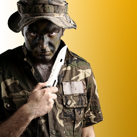 portrait of young soldier with knife and hat against yellow backgroundの写真素材