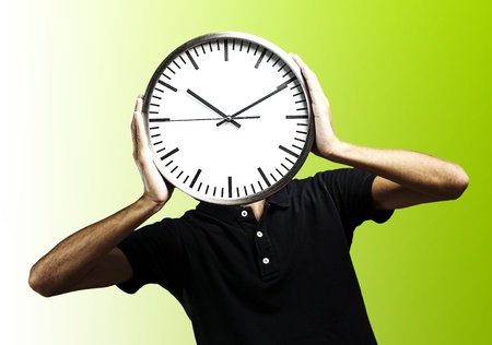 young man covering his face with a clock over green backgroundの写真素材