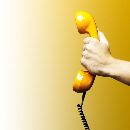 Hand holding vintage telephone receiver isolated over yellow backgroundの写真素材