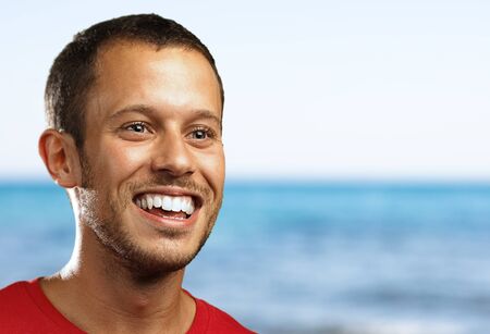 young man smiling against a beach backgroundの写真素材