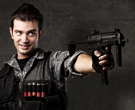 portrait of young soldier aiming with rifle against a grunge wall