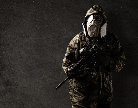 portrait of young soldier with rifle and gas mask against a grunge wallの写真素材