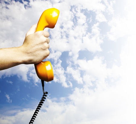 hand holding a vintage telephone against a blue sky backgroundの写真素材