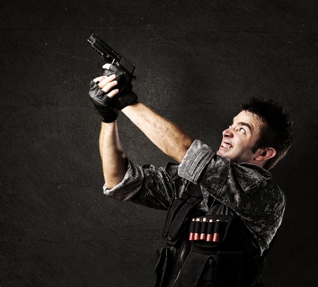 portait of young soldier aiming with gun against a grunge wall