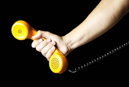 hand holding a yellow vintage telephone over black backgroundの写真素材