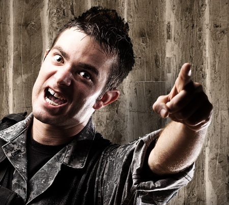 portrait of young soldier pointing with finger against a wooden wall