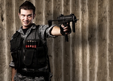 portrait of young soldier aiming with rifle against a grunge wooden wall