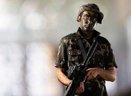 portrait of young soldier holding rifle against aa abstract background
