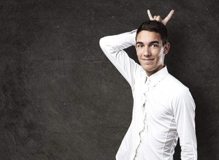 portrait of handsome young man doing horn symbol against a grunge wall