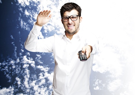 portrait of angry young man changing channel with tv control against a blue sky backgroundの写真素材