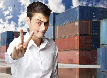 young man gesturing good at harbor against a ship containersの写真素材