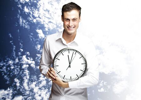 portrait of young man holding clock against a cloudy sky backgroundの写真素材