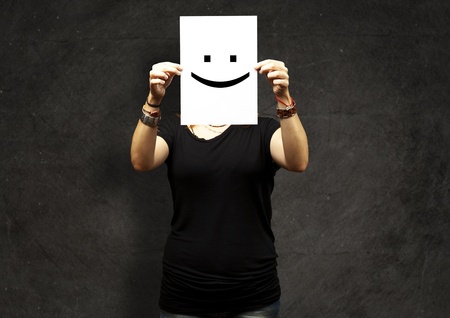 Woman showing a blank paper with a smile emoticon in front of her face against a grunge wallの写真素材