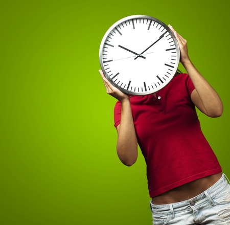 woman holding clock in front of head against a green backgroundの写真素材