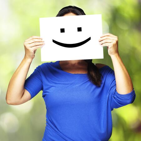 Woman showing a happy emoticon in front of face against a nature backgroundの写真素材
