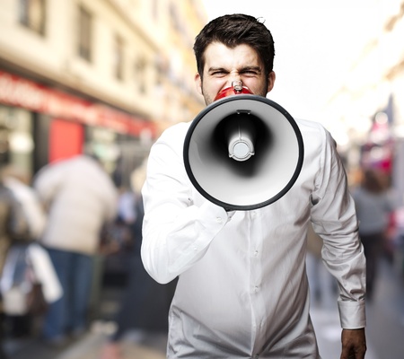 young man shouting through a megaphone against a street backgroundの写真素材