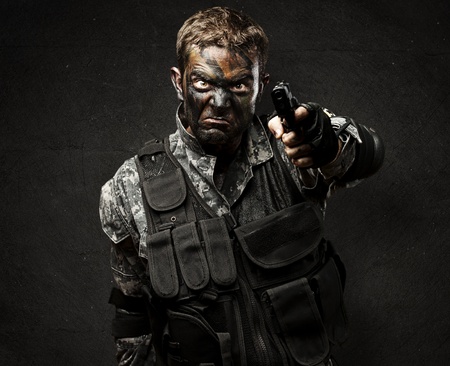 portrait of angry solider with urban camouflage pointing with gun against a grunge wallの写真素材