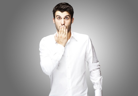 portrait of young man covering his mouth with hand over greyの写真素材