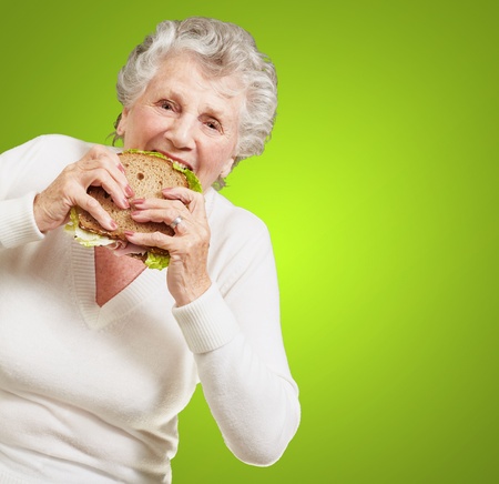 portrait of senior woman eating vegetal sandwich over green backgroundの写真素材