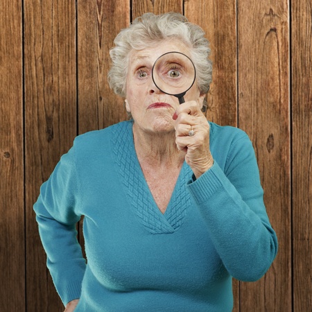 portrait of senior woman looking through a magnifying glass against a wooden wallの写真素材