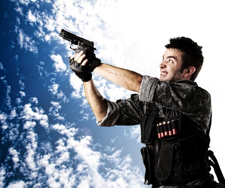 portait of young soldier aiming with gun against a cloudy sky background