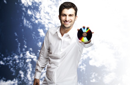 portrait of a handsome young man holding cd indoor against a cloudy sky backgroundの写真素材