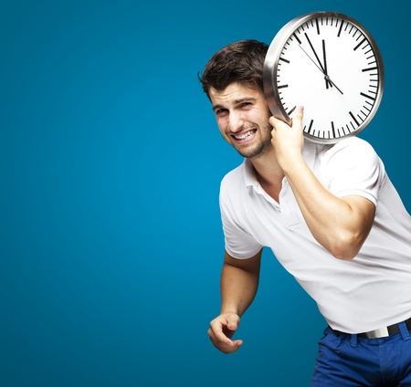 young man holding a clock on his back against a blue backgroundの写真素材