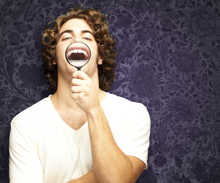 portrait of young man with magnifying glass showing his teeths against a vintage wallの写真素材