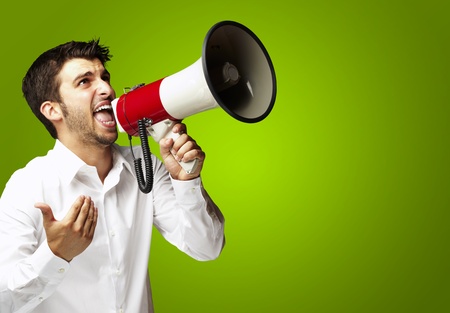 portrait of young man shouting with megaphone over green backgroundの写真素材