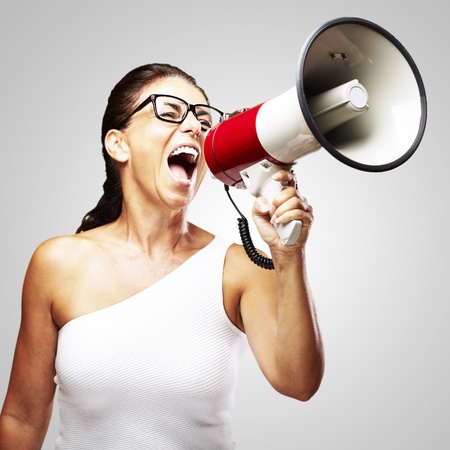 portrait of middle aged woman shouting using megaphone over grey backgroundの写真素材