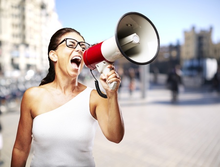 young woman shouting through a megaphone against a street backgroundの写真素材