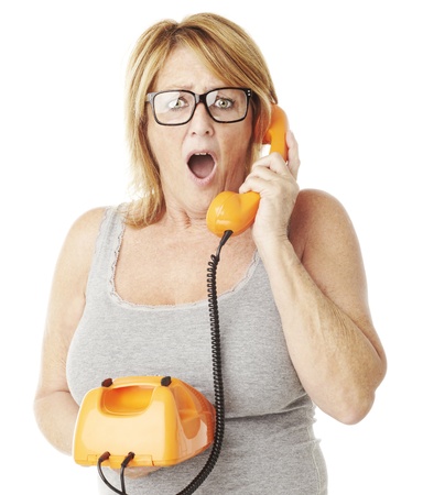 portrait of middle aged woman surprised talking on vintage telephone over whiteの写真素材
