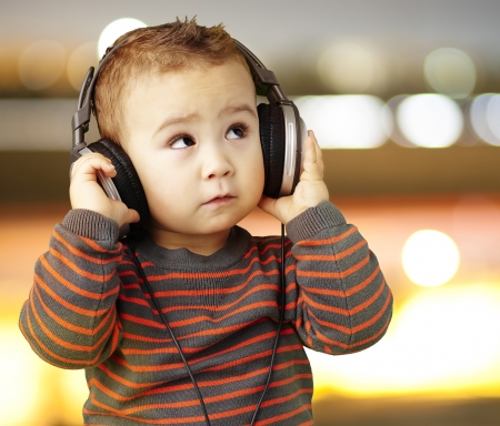 young boy wearing headphones and looking up against a city by nightの写真素材