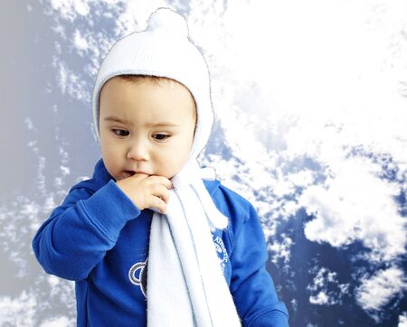 young boy with his finger in his mouth thinking against a cloudy sky backgroundの写真素材