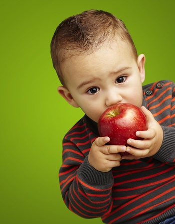 young boy tasting a red apple against a green backgroundの写真素材