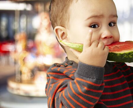 sweet boy tasting a watermelon slice against a carousel backgroundの写真素材