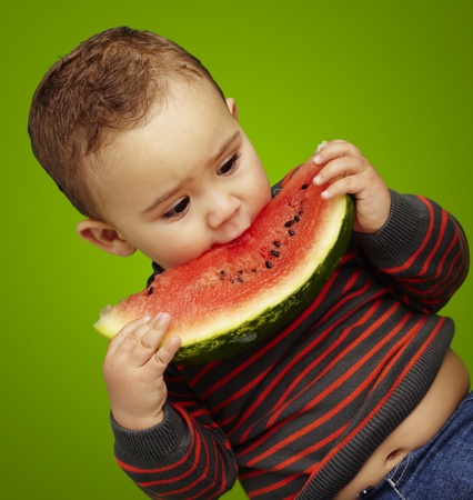 boy eating a watermelon slice against a green backgroundの写真素材
