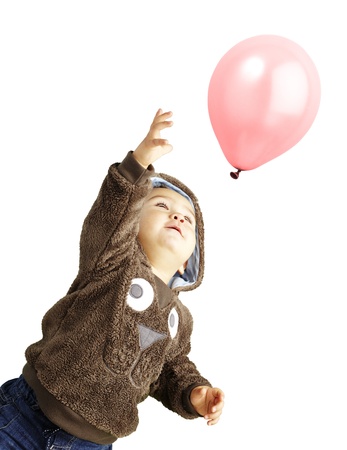 young boy trying to catch a pink balloon against a white backgroundの写真素材