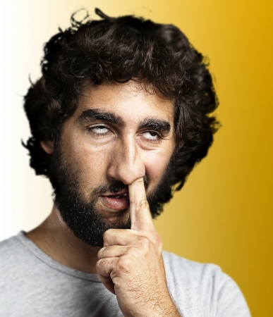 young man sticking his finger in his nose against a yellow backgroundの写真素材