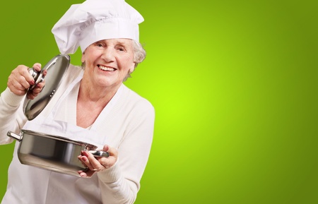 portrait of cook senior woman opening sauce pan over greenの写真素材