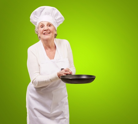 portrait of a friendly cook senior woman holding pan over green backgroundの写真素材