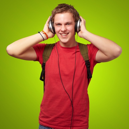 portrait of cheerful young student listening music with headphones over greenの写真素材